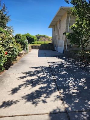 A concrete pathway leading to a building with a brick facade, a gated entrance, and a stone wall.