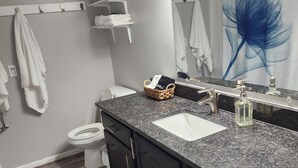 Un bagno con un lavandino bianco, mobiletti scuri, un portascopevoli, un WC e una tenda da doccia con motivo floreale blu.
