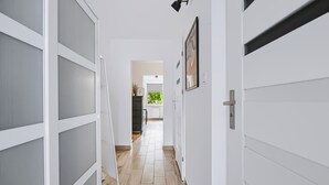 Un pasillo con puertas blancas, una lámpara negra y un cuadro en la pared.