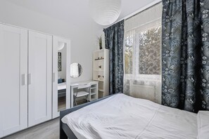 Un dormitorio con cama, escritorio, armario y ventana con cortinas.