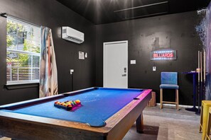 Ein Billardraum mit Pooltisch, Spielstöcken und einer Neonreklame.