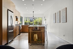 Een moderne keuken met een roestvrijstalen koelkast, houten keukenkastjes, een centraal eiland met een spoelbak en uitzicht op groen.