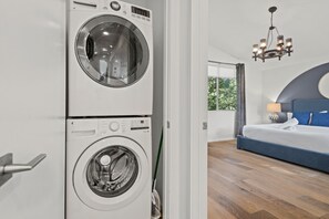 Een kamer met een wasmachine, een bed met een blauw hoofdeinde en een kroonluchter.