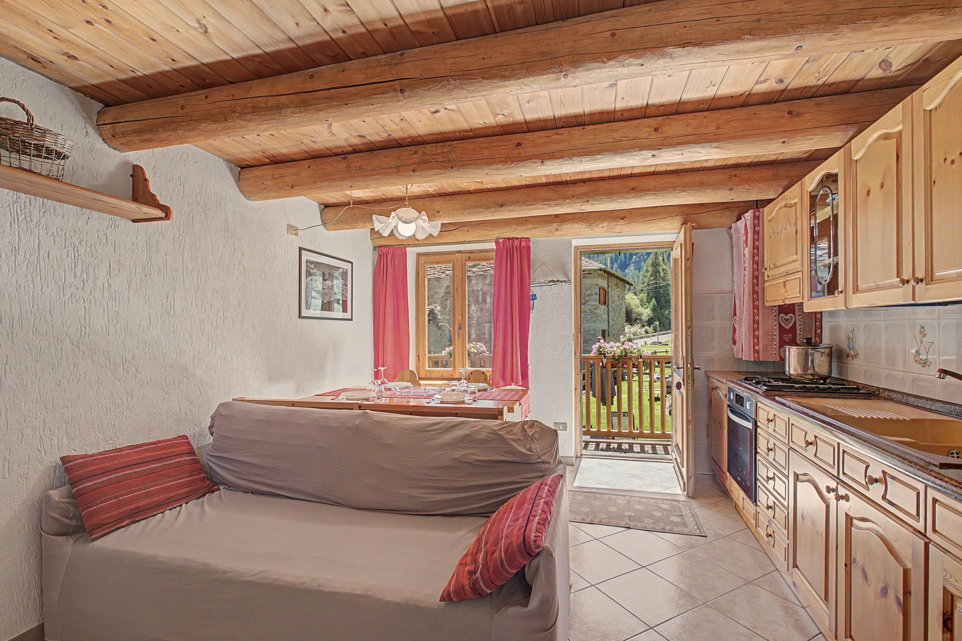Una stanza accogliente con soffitto in legno, un divano, un tavolo da pranzo per due persone e una cucina con mobili in legno.