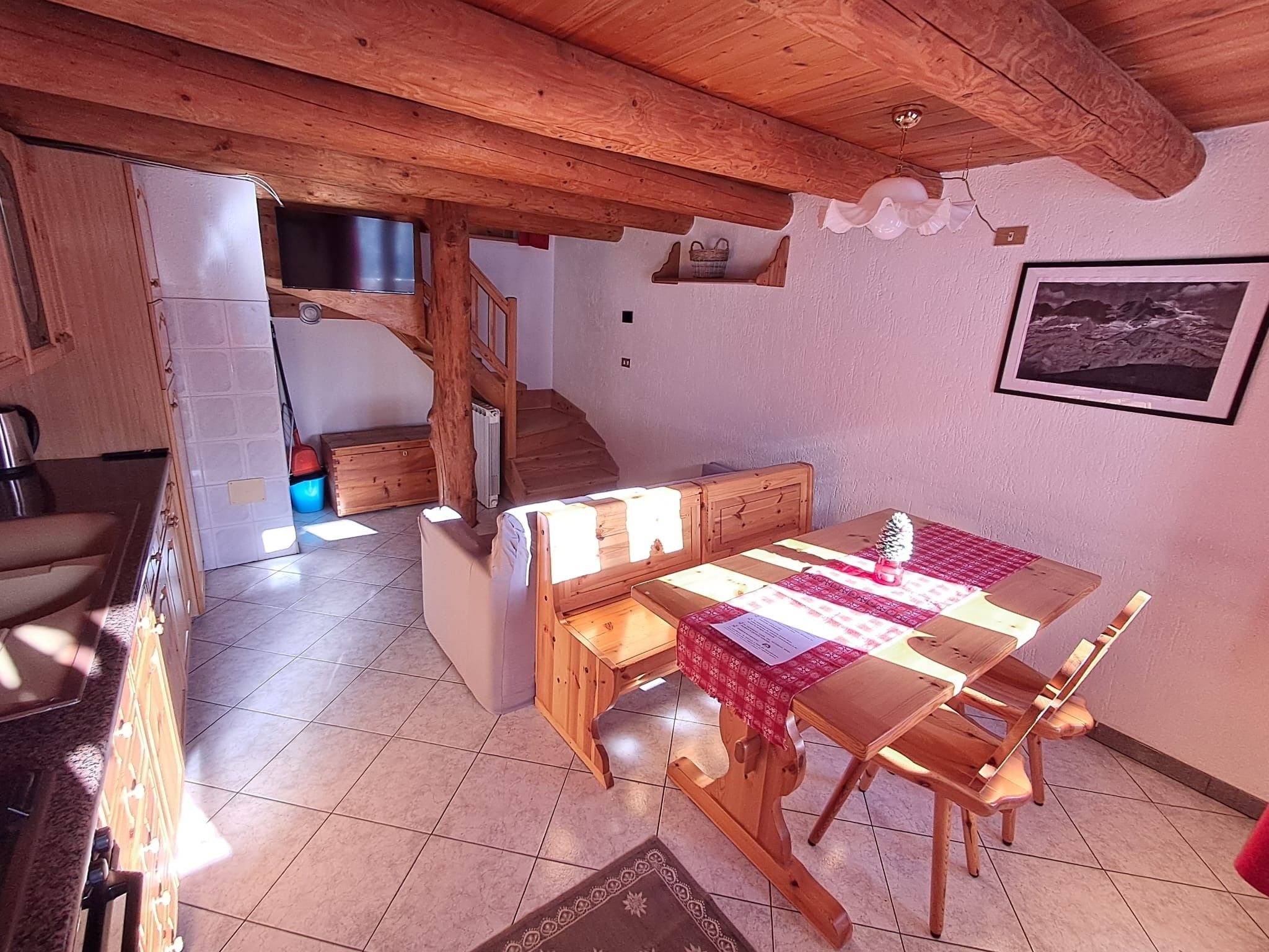Un ambiente rustico con un tavolo da pranzo in legno, sedie, una scala e un angolo cottura.