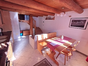 Un ambiente rustico con un tavolo da pranzo in legno, sedie, una scala e un angolo cottura.