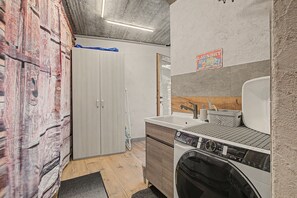 Una lavanderia con lavatrice, lavandino e mobiletto in legno.