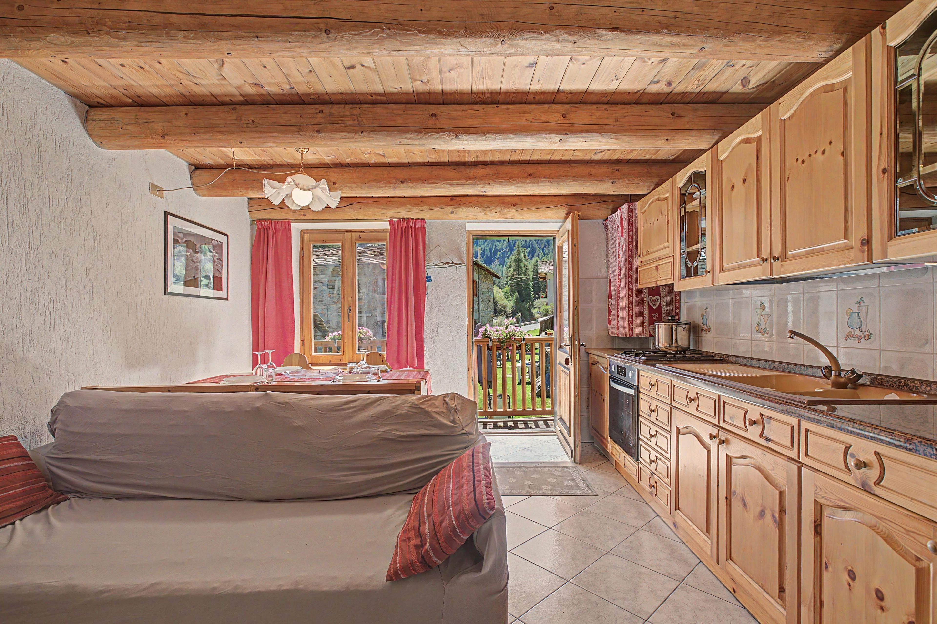 Una stanza accogliente con soffitto in legno, un divano, un tavolo da pranzo con sedie e una cucina con pensili in legno.