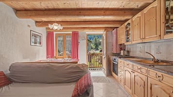 Una stanza accogliente con soffitto in legno, un divano, un tavolo da pranzo con sedie e una cucina con pensili in legno.