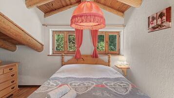 Una camera da letto con soffitto in legno, un letto con copripiumino decorato, un comodino con una lampada e una finestra vista alberi.