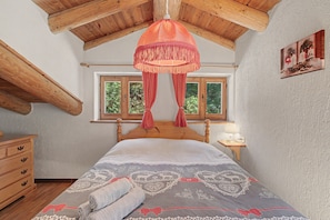 Una camera da letto con soffitto in legno, un letto con copripiumino decorato, un comodino con una lampada e una finestra vista alberi.