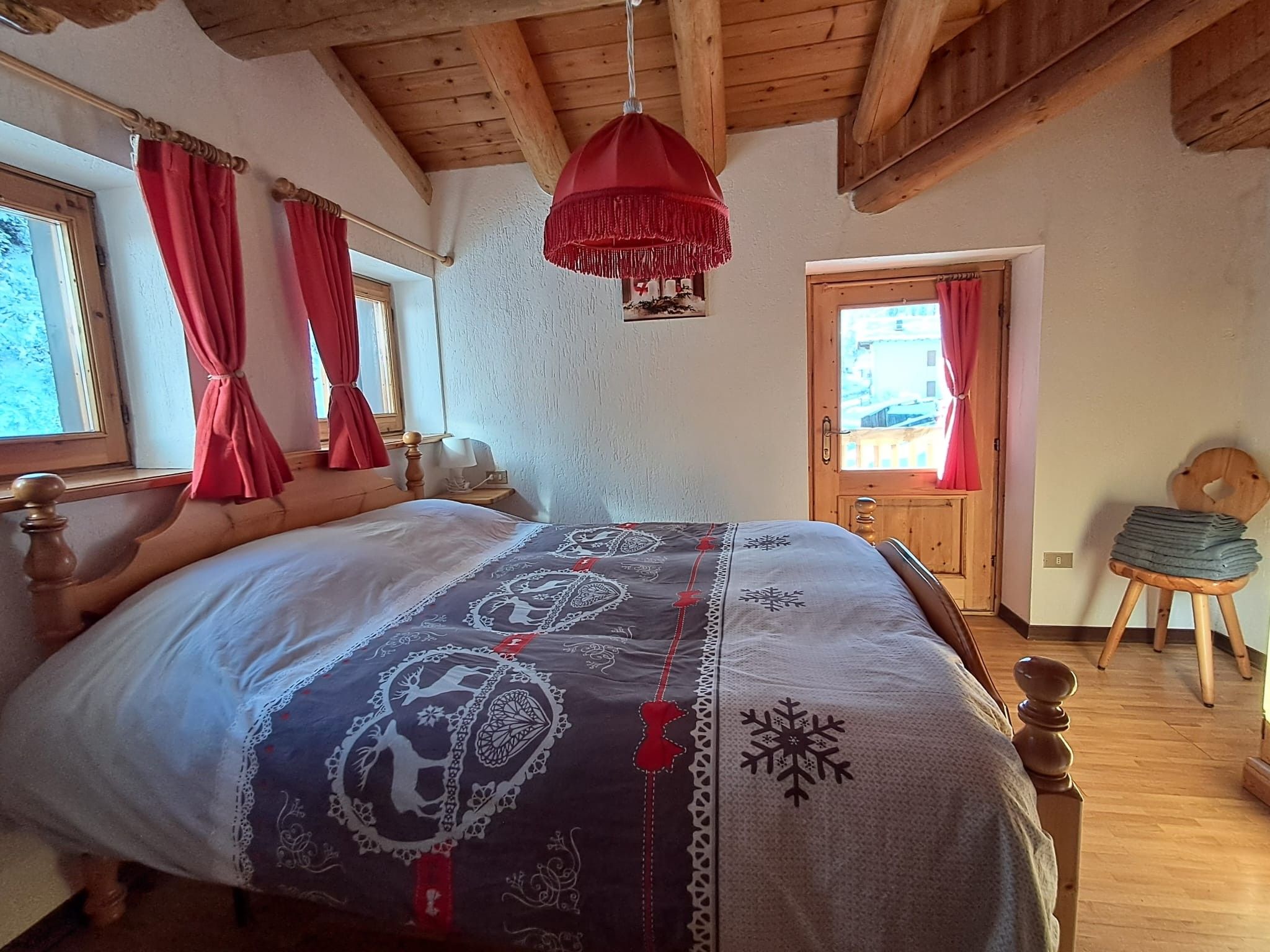 Camera da letto con un letto in legno, una lampada a sospensione rossa e vista all'esterno attraverso una finestra con tende rosse.