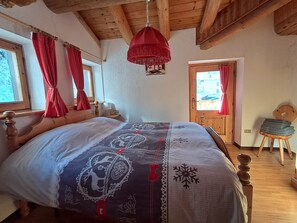 Camera da letto con un letto in legno, una lampada a sospensione rossa e vista all'esterno attraverso una finestra con tende rosse.