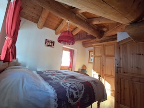 A bedroom with a wooden ceiling, a bed with a patterned bedspread, a hanging red lamp, and wooden furniture.