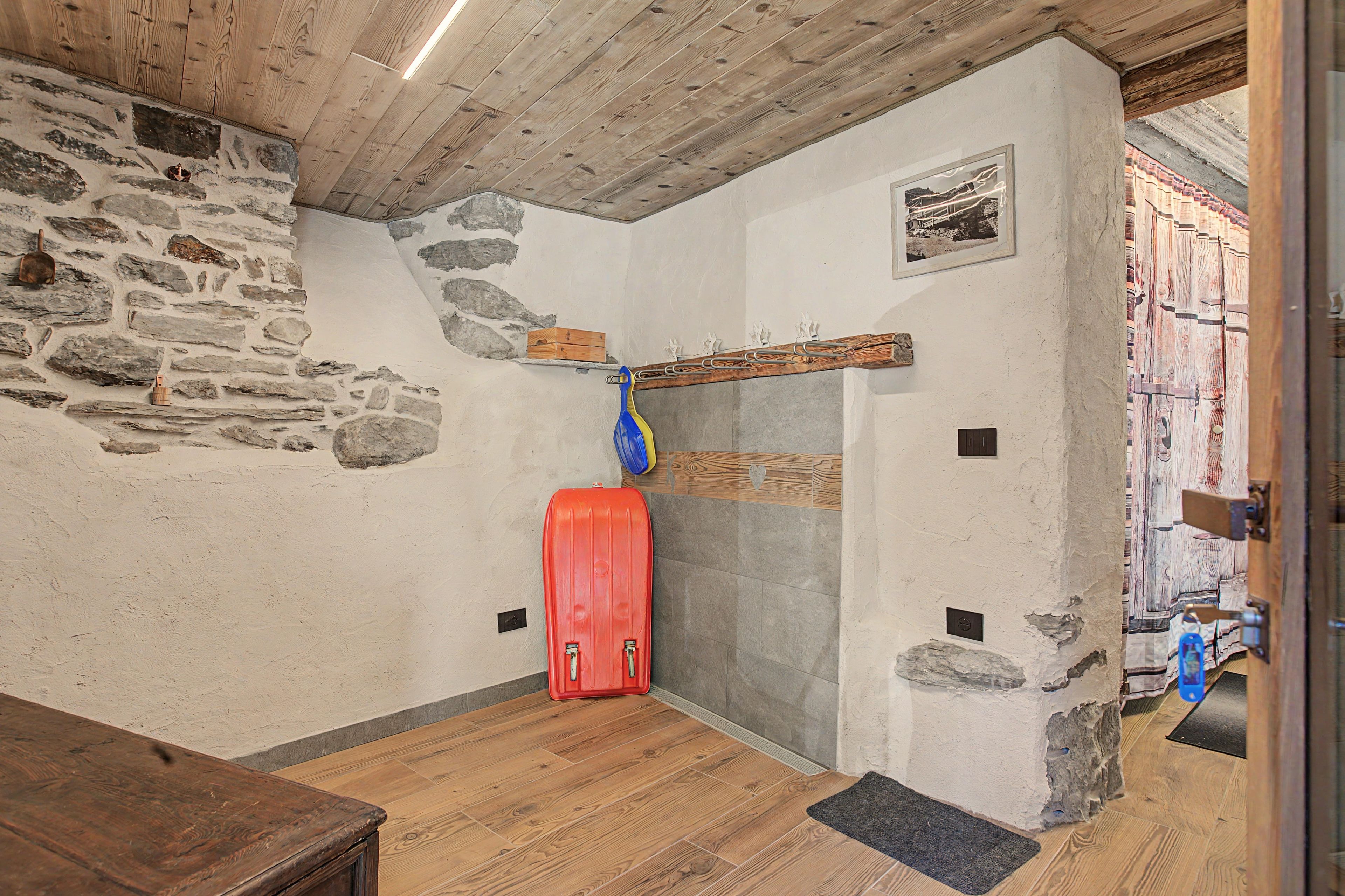 Un interno rustico con pareti in pietra, soffitto in legno e una valigia rossa sul pavimento.