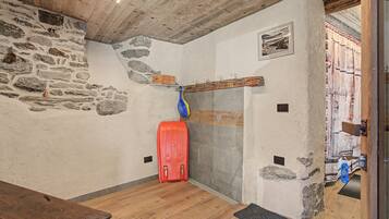 Un interno rustico con pareti in pietra, soffitto in legno e una valigia rossa sul pavimento.