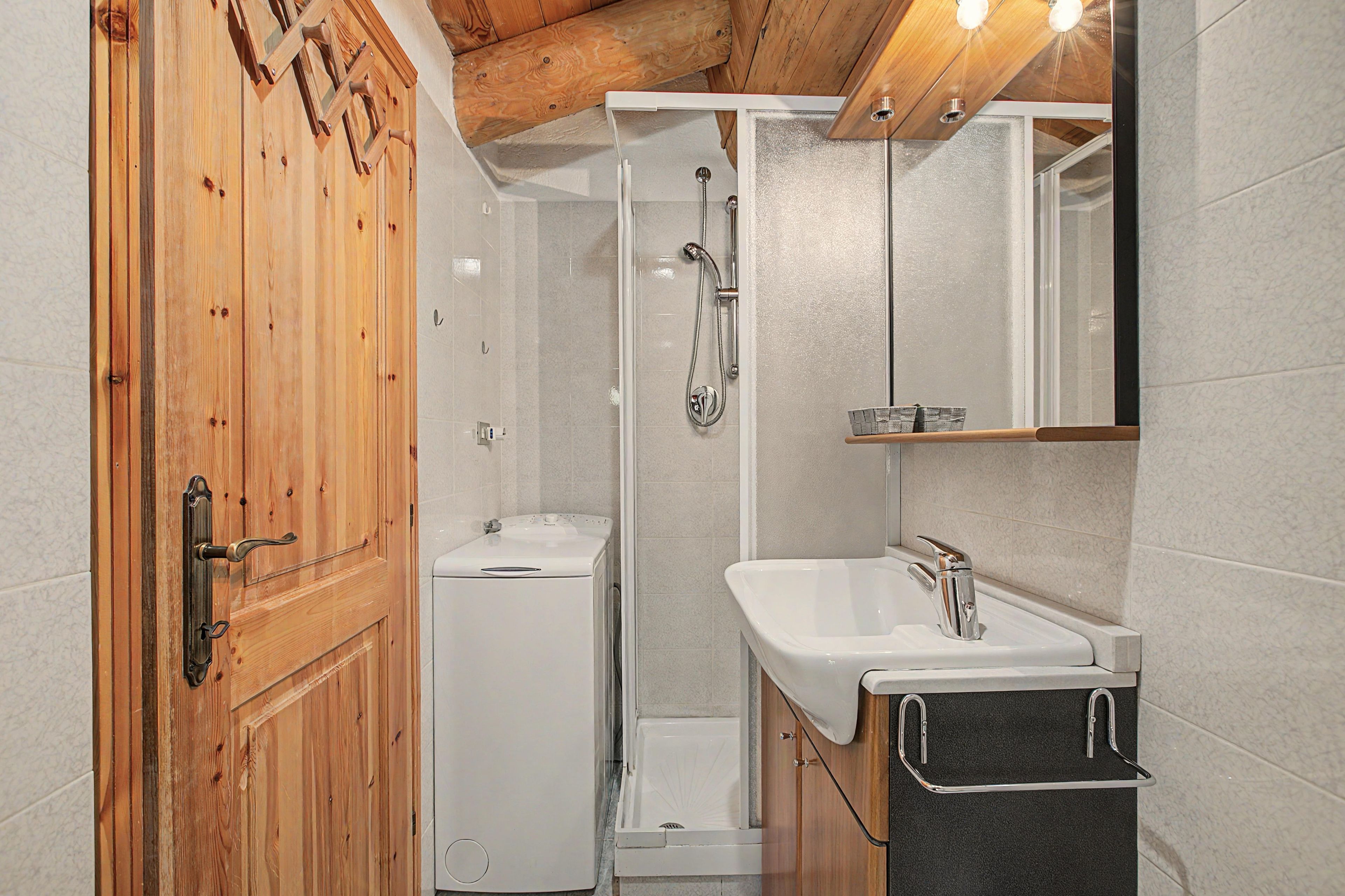 Ein Badezimmer mit Holztür, einer weißen Waschmaschine, einer Dusche und einem Waschbecken mit Handtuchhalter.