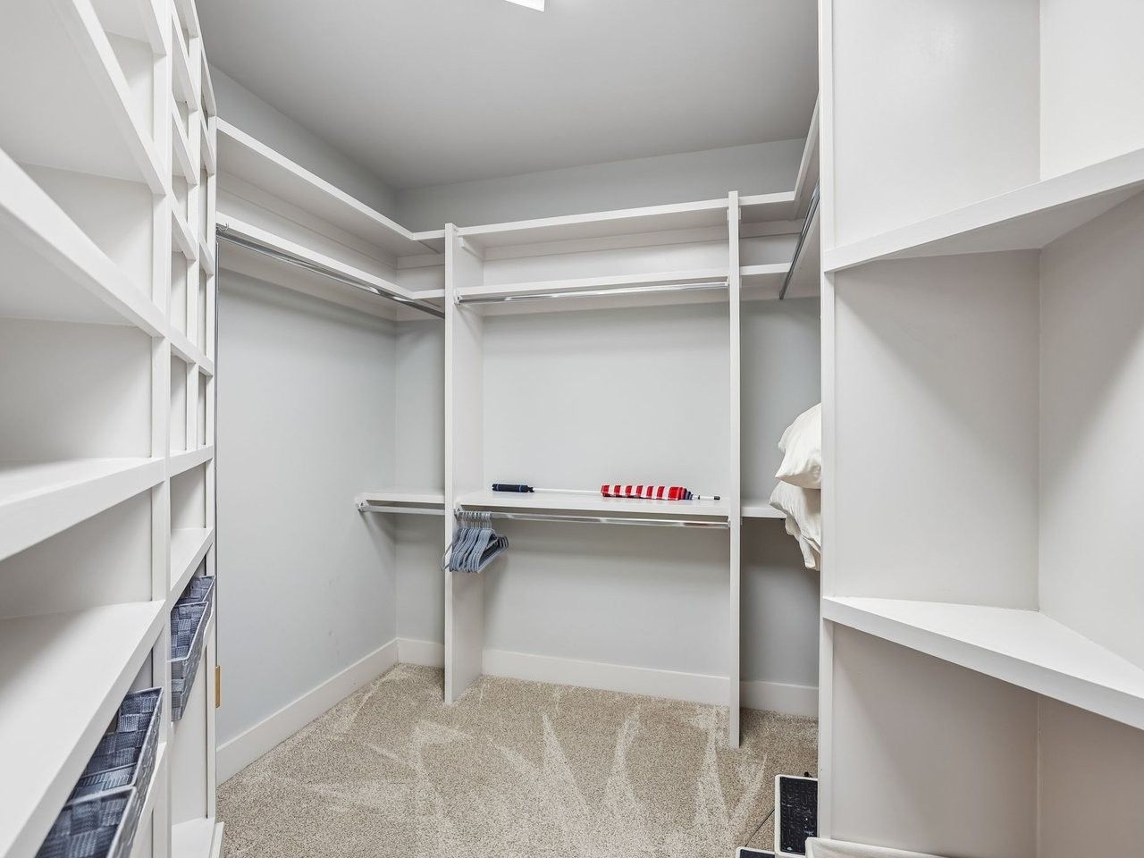 A walk-in closet with white shelving units and a carpeted floor.
