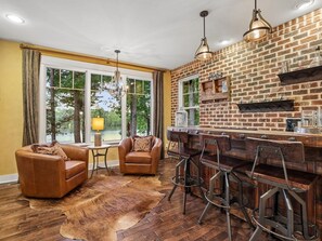 Une cuisine moderne avec un mur en briques, des tabourets de bar et une grande fenêtre donnant sur un paysage naturel.