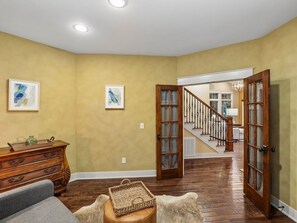 Ein geräumiges Wohnzimmer mit Holzböden, einer Holzkommode und einem grauen Sofa. Eine Treppe führt zu einer oberen Ebene.