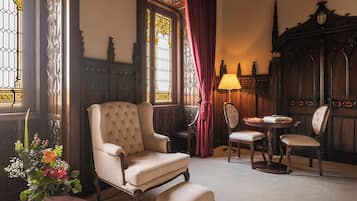 Una habitación con un sillón grande, una mesa con sillas, un florero con flores y una lámpara.