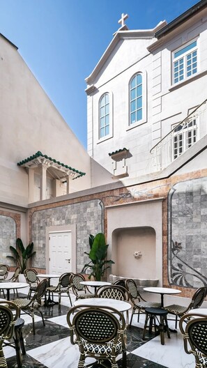Un patio con mesas al aire libre y un edificio con una cruz en la parte superior.