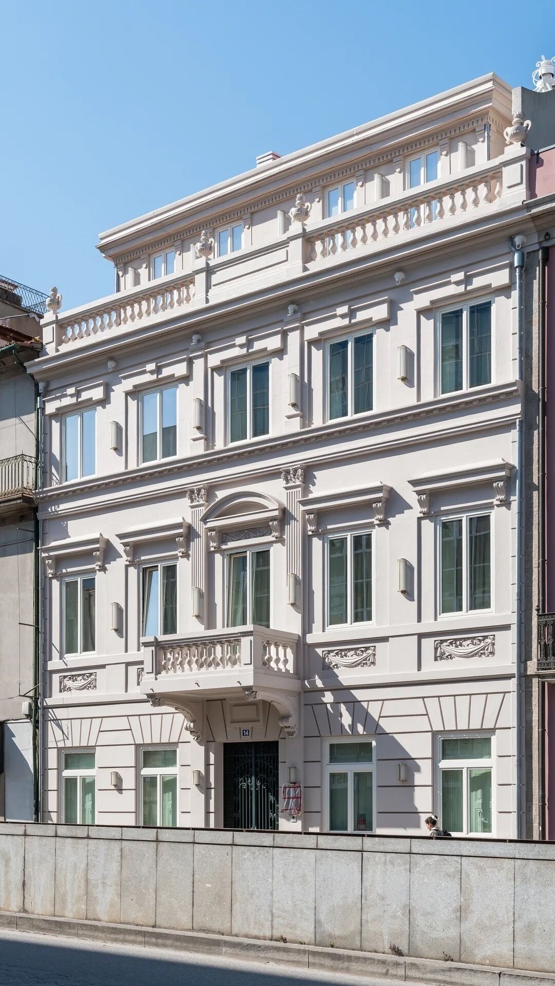 Ein mehrstöckiges Gebäude im klassischen Stil, mit einem Balkon mit aufwendigen Balustraden und einem großen Eingang mit dekorativem Bogen.