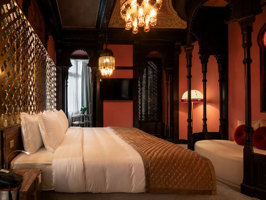 Una habitación de hotel con una cama grande, un candelabro y detalles arquitectónicos ornamentados.