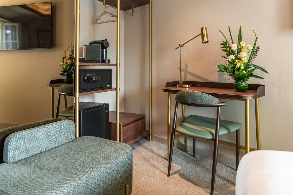 Une chambre d’hôtel comprenant un lit, un bureau avec un ordinateur, une chaise, une petite table, une lampe et une plante décorative.