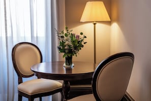 Una mesa redonda con dos sillas, un florero y una lámpara de pie en una habitación con ventana y cortinas.