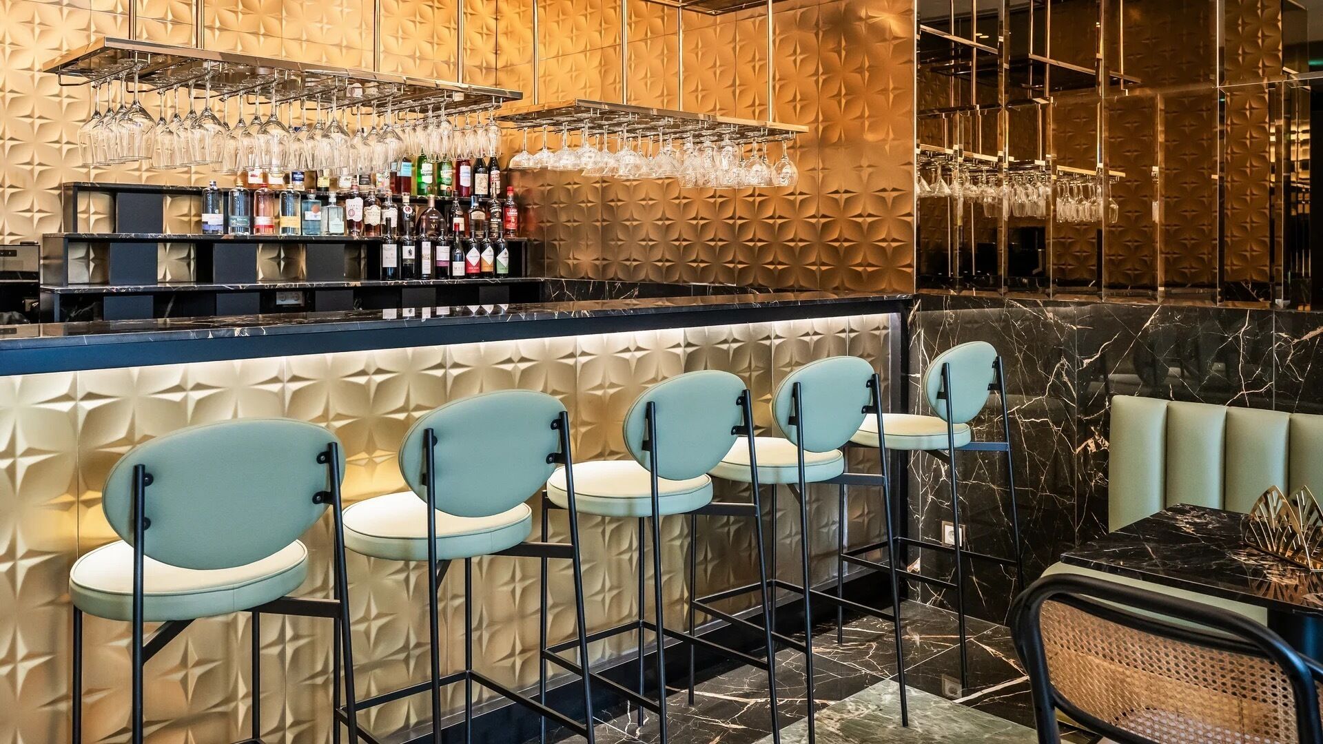 Zona de bar con pared decorada, una estantería para vinos y taburetes.
