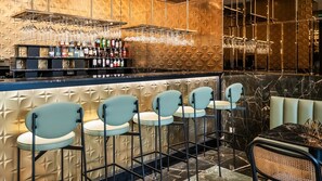 Zona de bar con pared decorada, una estantería para vinos y taburetes.