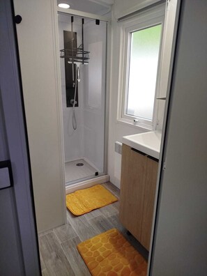 Un baño pequeño con cabina de ducha, ventana y lavamanos.