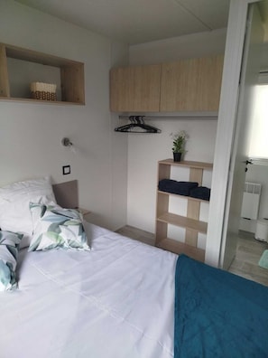 Een slaapkamer met een bed, een nachtkastje, een hanglamp, een garderobe en een klein plankje met een plantje.