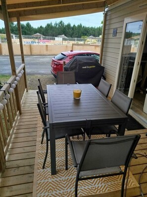 Un patio exterior con mesa y sillas, una parrilla cubierta y vistas a un estacionamiento.