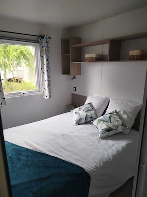 Un dormitorio con cama, ventana con cortinas, mesita de noche y estante con cestas.