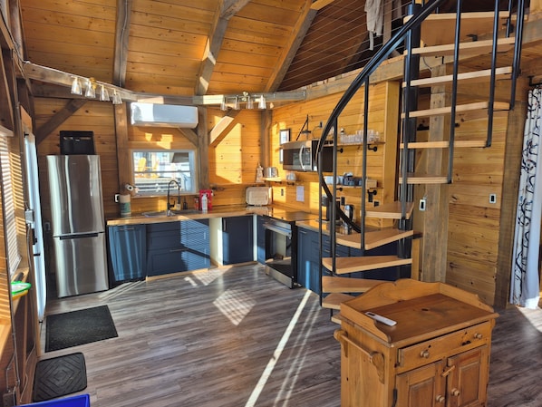 A compact kitchen with modern appliances, a wooden interior, and a spiral staircase.