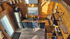 Una cocina compacta con refrigerador de acero inoxidable, gabinetes de madera y un ventanal que proporciona luz natural.