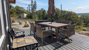 Une terrasse extérieure avec une table et des chaises en bois, un parasol et une vue sur des arbres et une étendue d’eau.