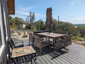 An outdoor deck with a wooden table and chairs, a patio umbrella, and a view of trees and a body of water.