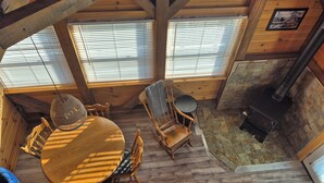 L’intérieur chaleureux d’un chalet avec une table à manger en bois, des chaises, un luminaire suspendu, une cheminée et un mur en pierre.