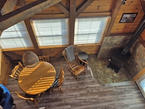 A cozy cabin interior with a wooden dining table, chairs, a hanging light fixture, a fireplace, and a stone wall.