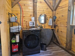 A compact, wooden cabin-style bathroom with a washing machine, a sink, and a mirror.