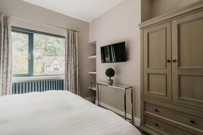 Ein Schlafzimmer mit einem Bett, einem Heizkörper, einem an der Wand montierten Fernseher, einer kleinen Topfpflanze und einem Holzschrank.