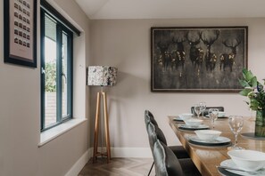 Ein Essbereich mit einem Holztisch, gedeckt für vier Personen, einer Stehlampe und einem gerahmten Kunstwerk an der Wand.