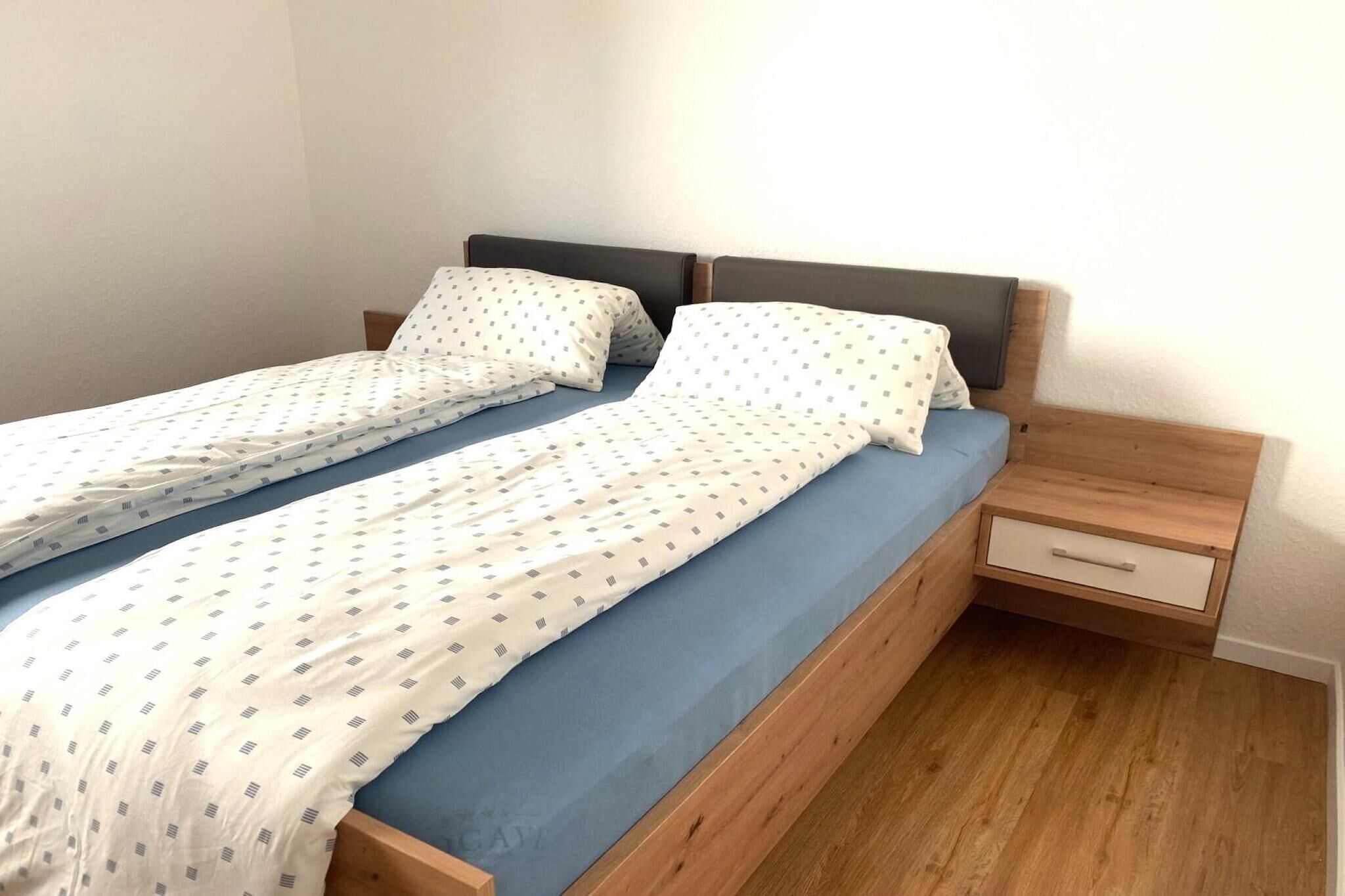 Un lit double avec un cadre en bois, deux oreillers, un protège-matelas bleu et une table de chevet avec un tiroir.