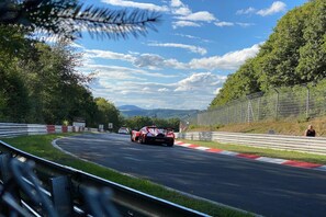 A race track with a car in motion, surrounded by greenery and a clear sky. - Apartment Spiegelkurve (Adenau)