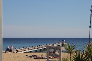 A beach with a wooden pier extending into the water, people sitting and walking on it, and a sign that reads 'SERVICE CONTINUED'. - Bright Apartment by the Ligurian sea (La croix-Valmer)