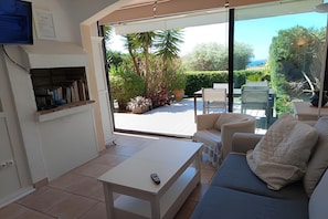 Een kamer met een bank, een tafel, een televisie en uitzicht op een tuin via een glazen deur.