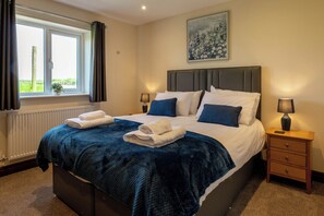 Ein ordentlich bezogenes Bett mit einer blauen Decke, zwei Nachttischlampen, einem Holznachttisch und einem Fenster mit Vorhängen.